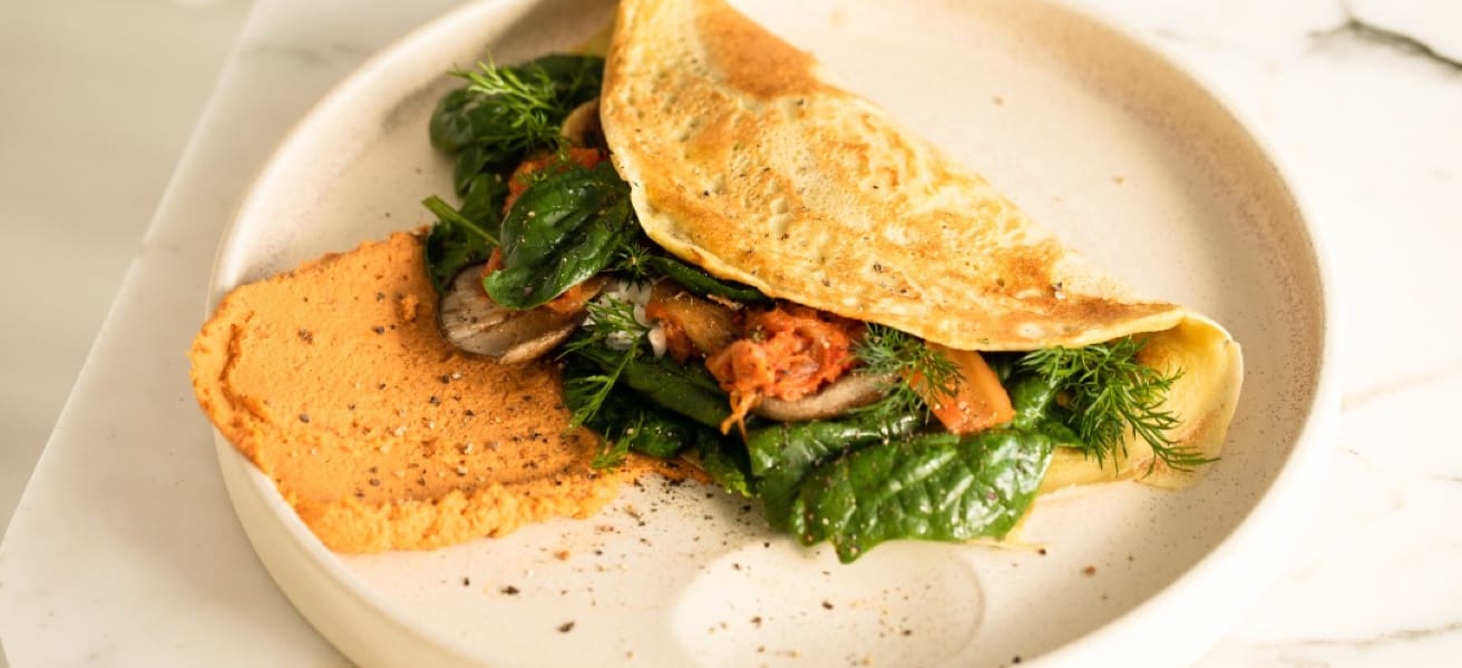 A picture of an omelelette on a plate that contains an absurd amount of spinach. There is also a sauce next to it.